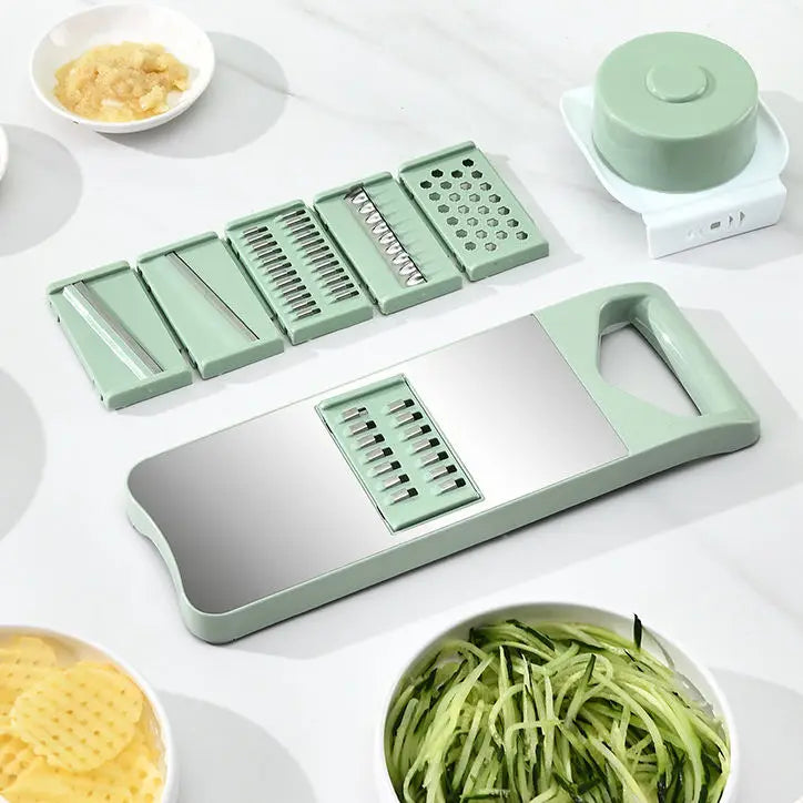 Green vegetable spiralizer with attachments on a white surface, surrounded by sliced vegetables.